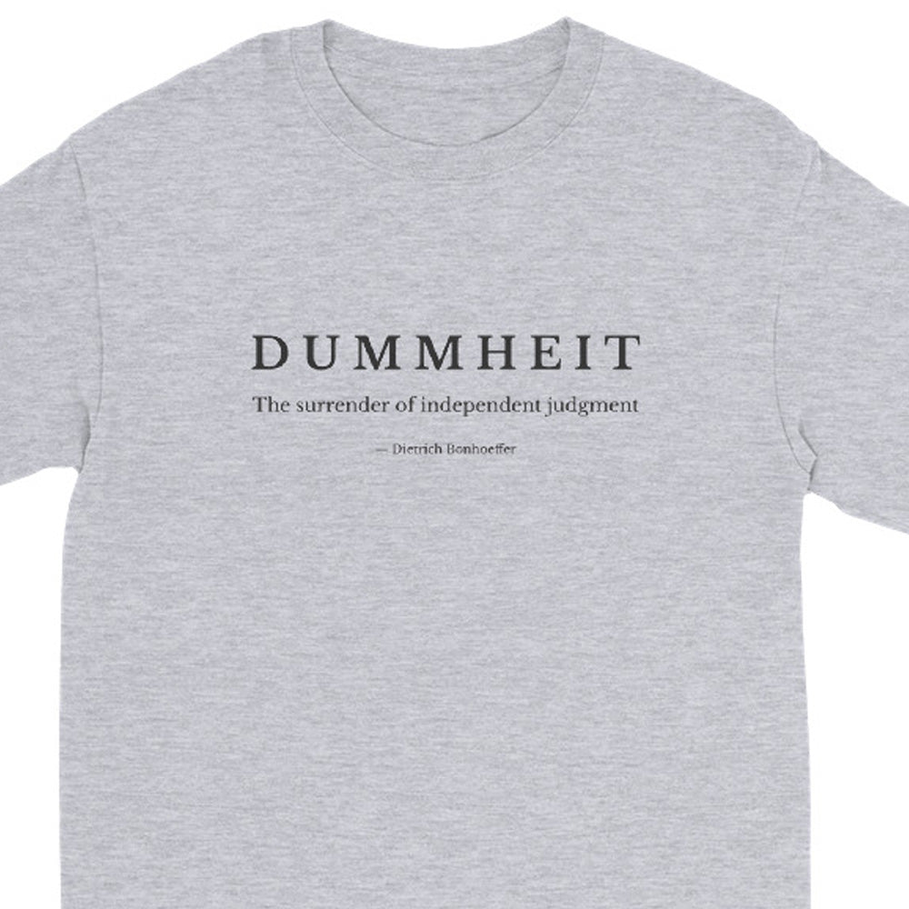 A sport grey crewneck long sleeve t-shirt featuring a black printed graphic on the chest. The graphic reads 'DUMMHEIT' in a serif font, followed by the subtitle 'The surrender of independent judgment' and a quote attribution to 'Derrick Deboncage'.