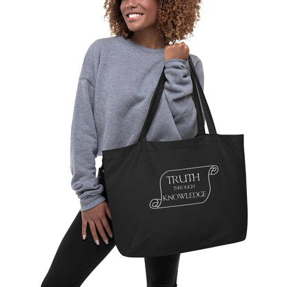 Person holding a black tote with the outline of a scroll with the words "Truth through Knowledge"